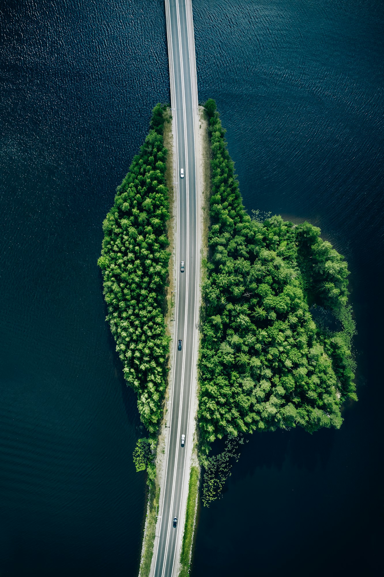 Aerial view of road through blue lakes or sea with green woods in Finland.